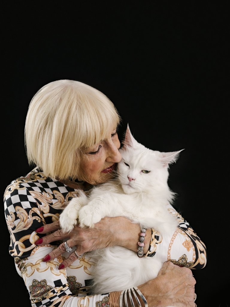 Woman embraces white cat against black backdrop.